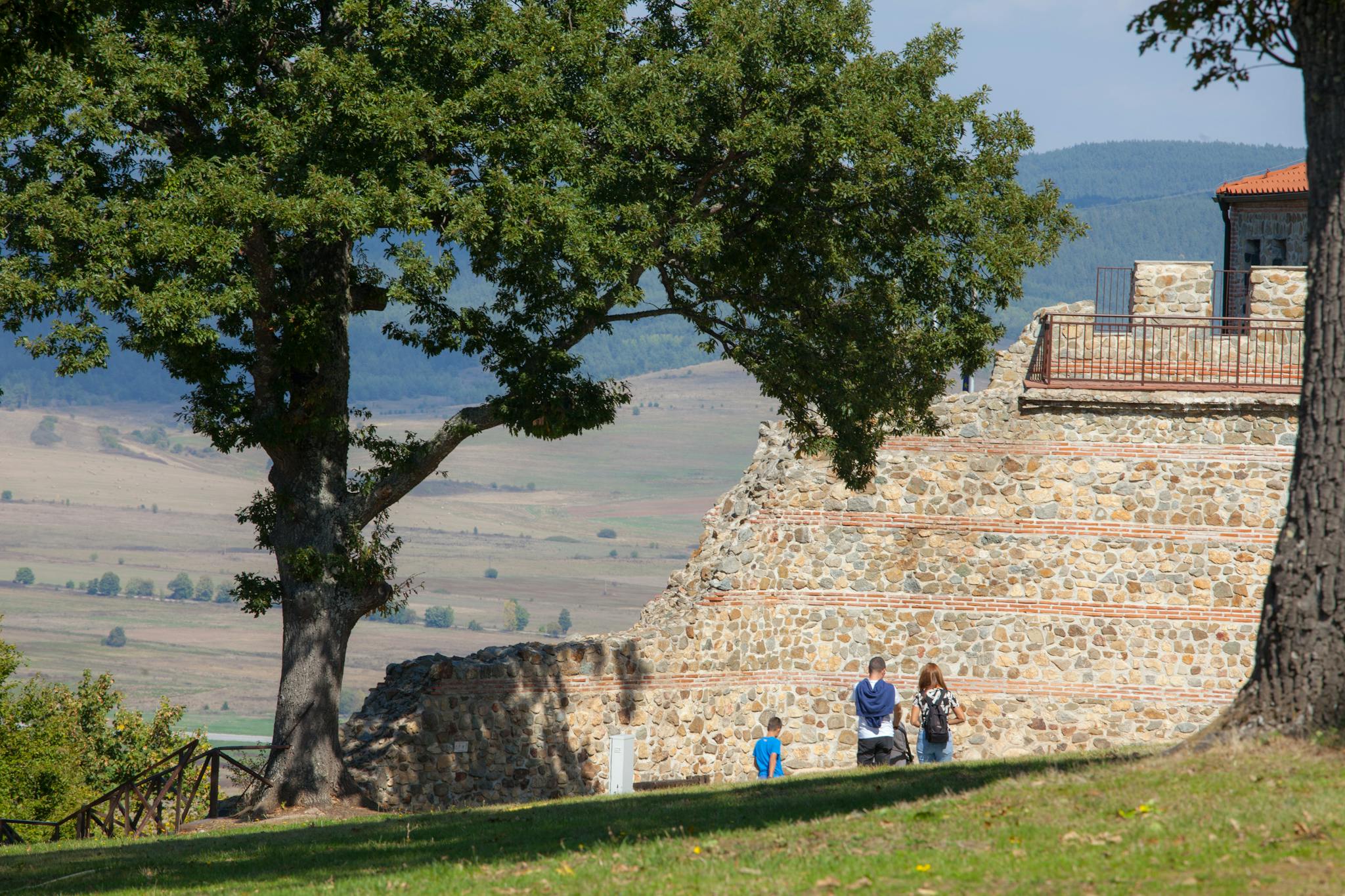 A family exploring ancient stone ruins in a picturesque, tree-lined countryside setting.